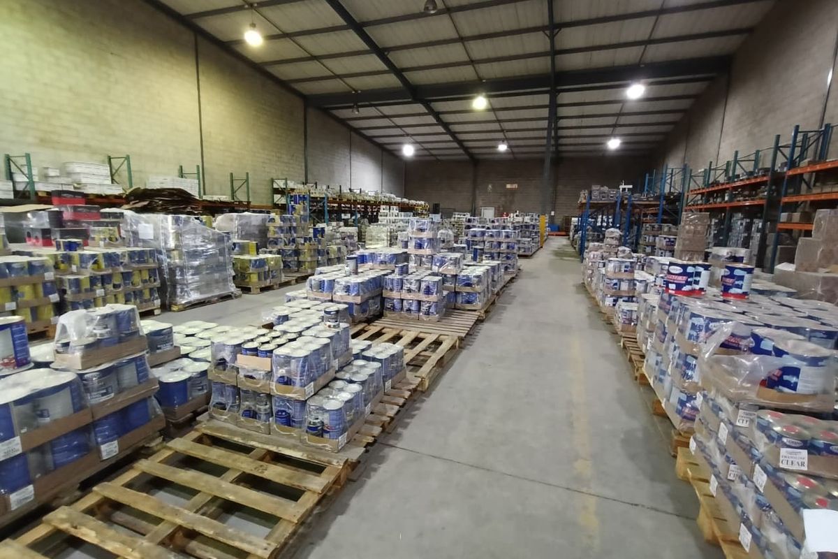 Spacious industrial warehouse featuring high ceilings with exposed steel trusses, concrete flooring, and functional overhead lighting, currently utilized for bulk storage.