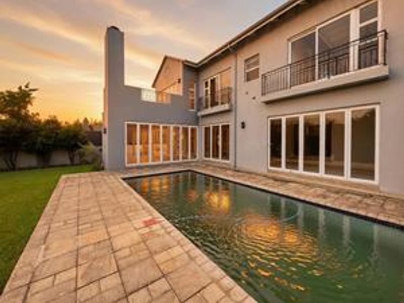 Rear exterior view of a two-story house featuring a swimming pool, paved patio area, and multiple sliding glass doors leading to the interior.