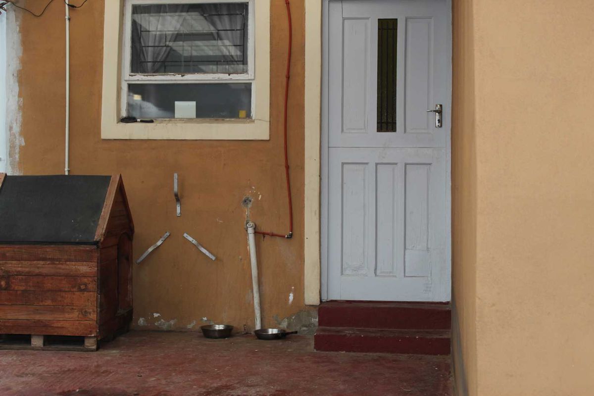 Rear exterior view showing a painted masonry wall, a single panel door, and concrete steps with visible signs of wear and surface-mounted conduit.