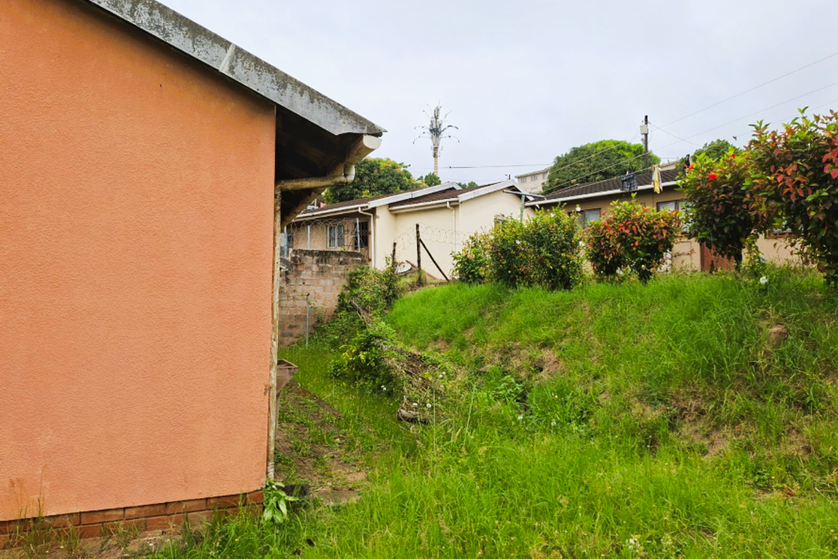 A view of the side and rear exterior of the property, featuring a grassed yard area and adjacent residential buildings.