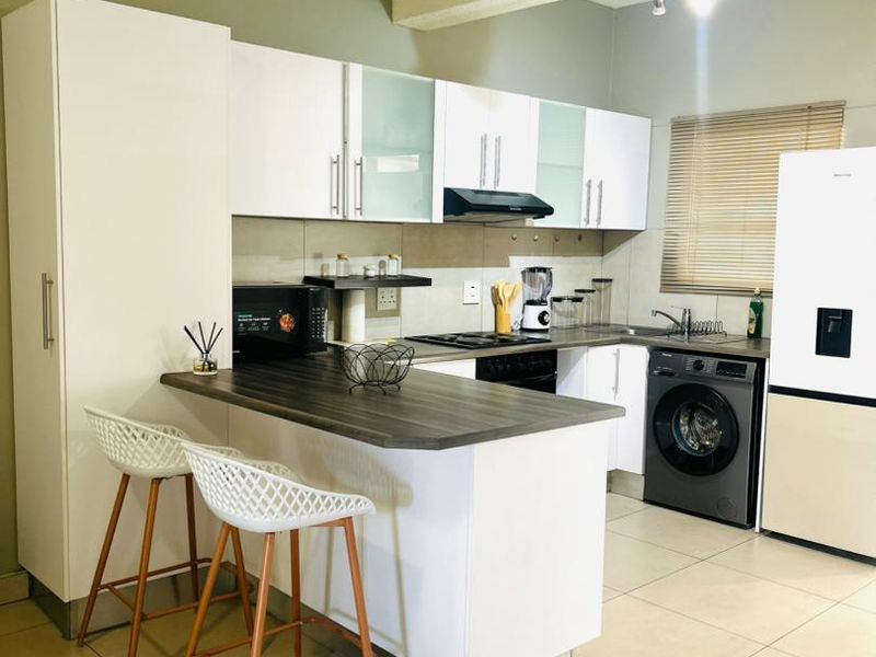Modern kitchen featuring white cabinetry, dark laminate countertops, a breakfast bar, integrated appliances, and tiled flooring with neutral wall tones.