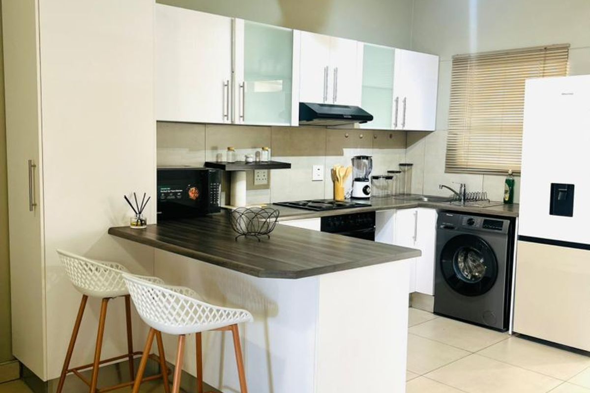 Modern kitchen featuring white cabinetry, dark laminate countertops, a breakfast bar, integrated appliances, and tiled flooring with neutral wall tones.