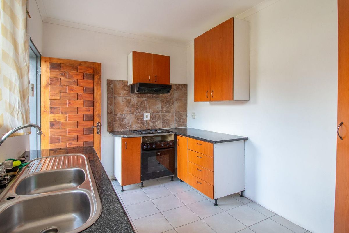 Functional kitchen featuring wood-look cabinetry, granite-style countertops, a built-in oven with hob, extractor fan, and a double stainless steel sink.