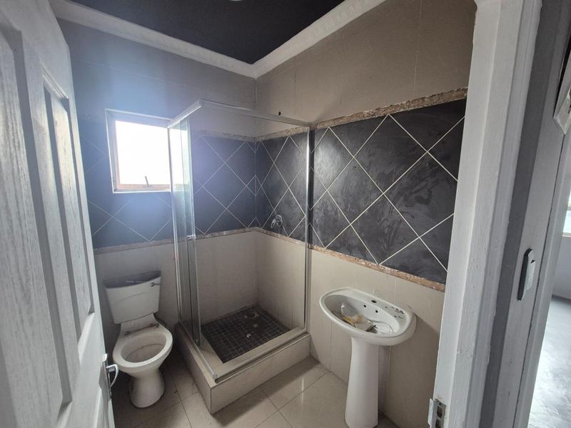 A compact bathroom featuring a pedestal basin, toilet, and a glass-enclosed shower with partially finished wall tiling.