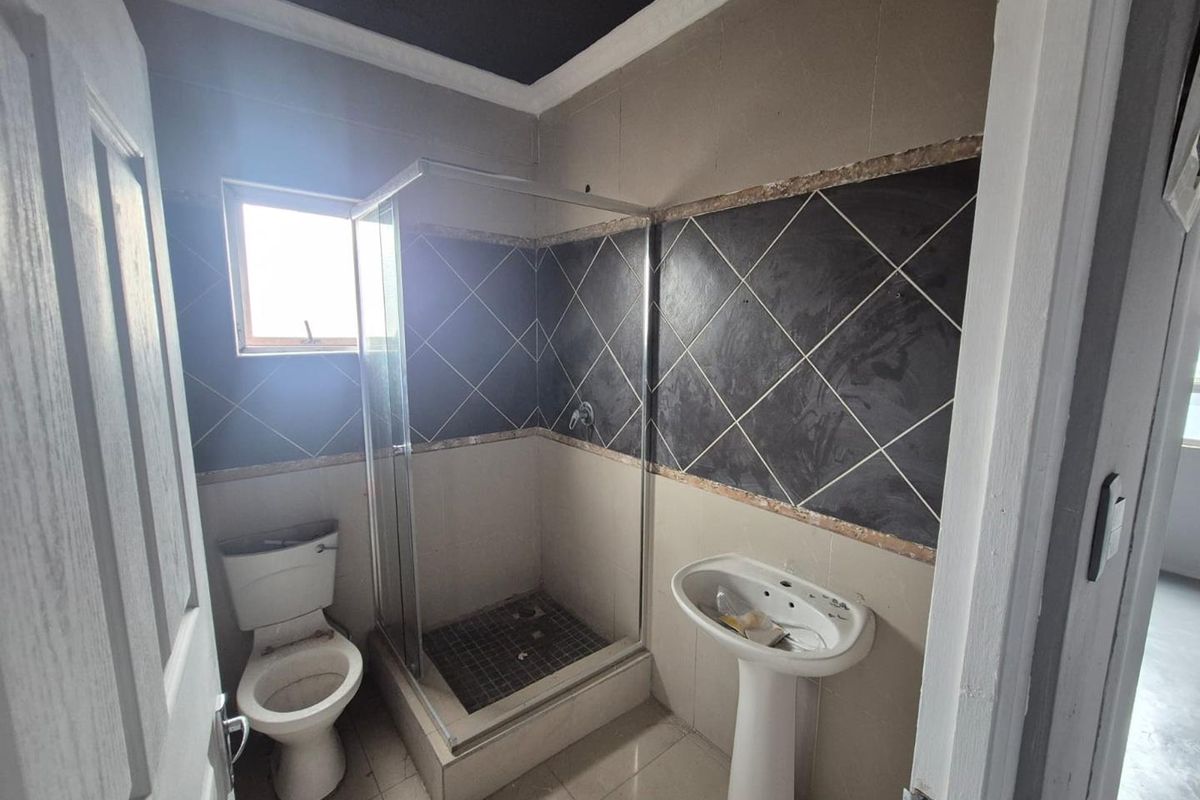 A compact bathroom featuring a pedestal basin, toilet, and a glass-enclosed shower with partially finished wall tiling.