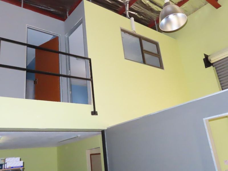 Open plan commercial space featuring a mezzanine level with metal railing, exposed industrial roof structure, and high ceilings with pendant lighting.