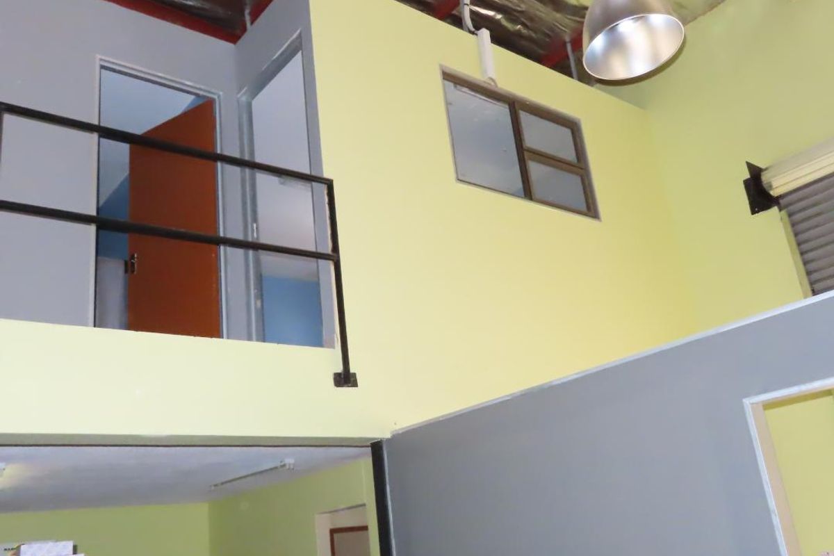 Open plan commercial space featuring a mezzanine level with metal railing, exposed industrial roof structure, and high ceilings with pendant lighting.