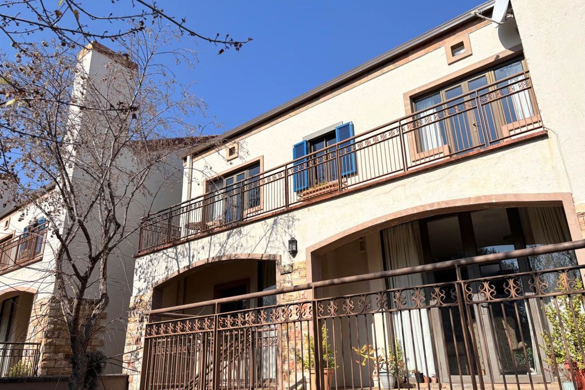 Exterior view of a townhouse featuring a covered patio, upper-level balcony with metal railings, stone cladding accents, and blue window shutters.