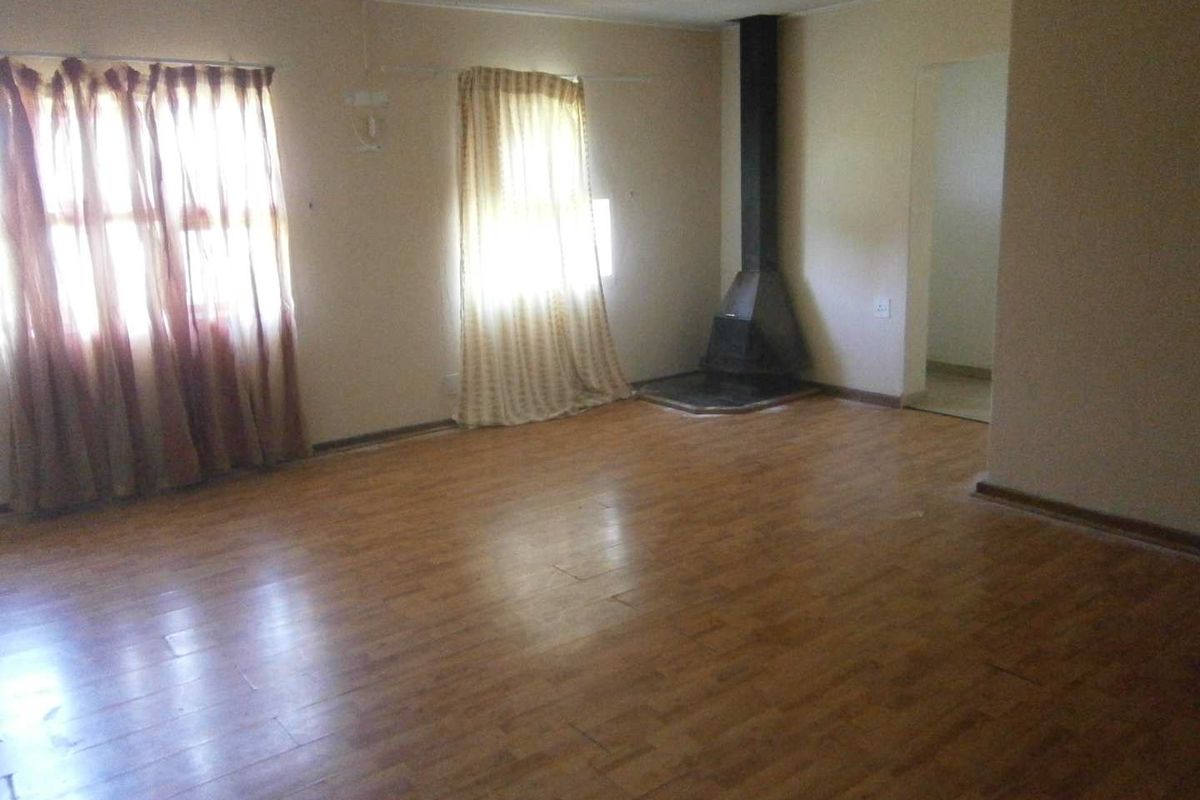 Spacious living room featuring wood-look laminate flooring and a built-in metal fireplace, offering a blank canvas for renovation.