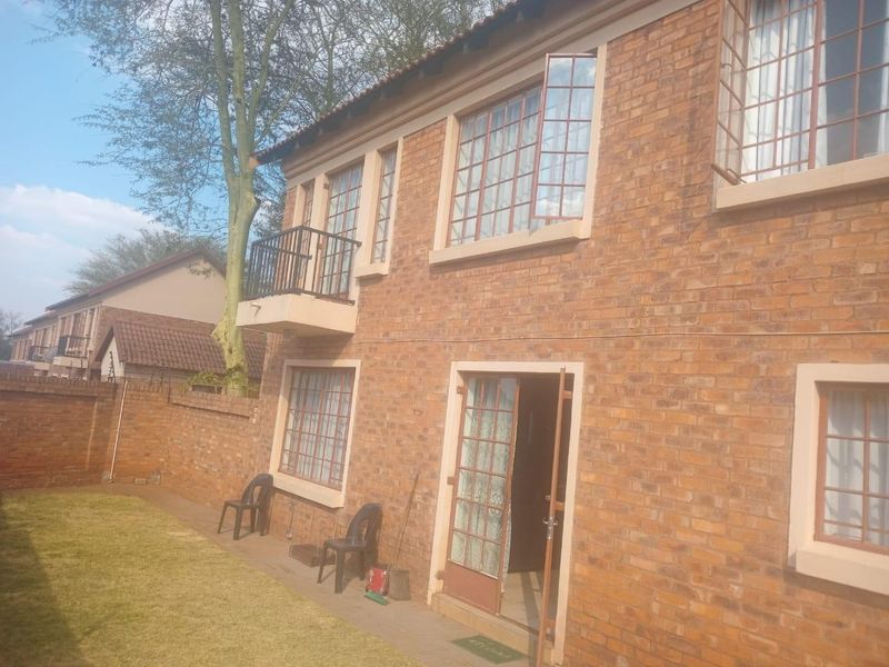 Rear view of a two-story face brick townhouse featuring a small balcony, security bars on windows, and a private garden area.