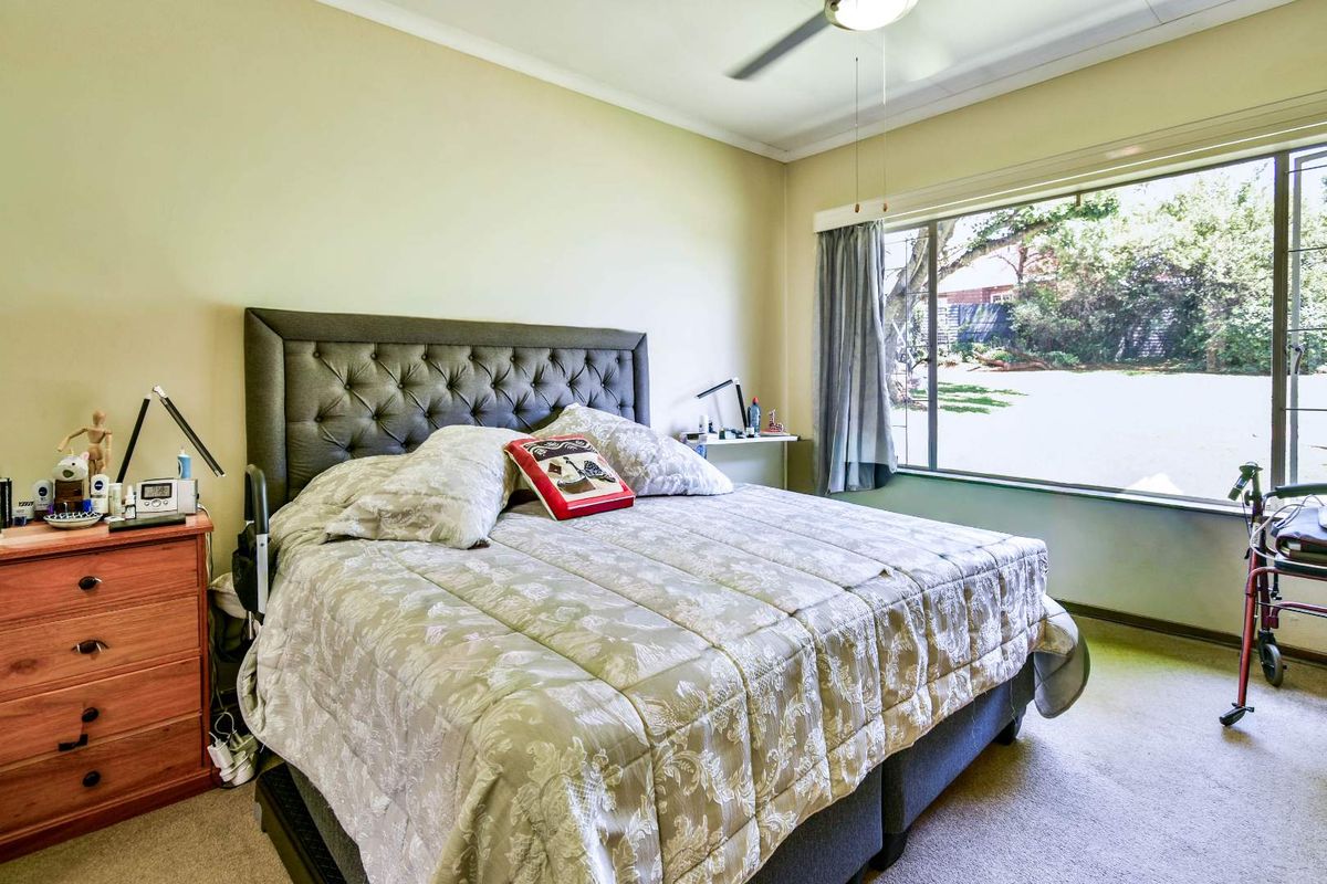A bedroom featuring a large window with garden views, a ceiling fan, and carpeted flooring.
