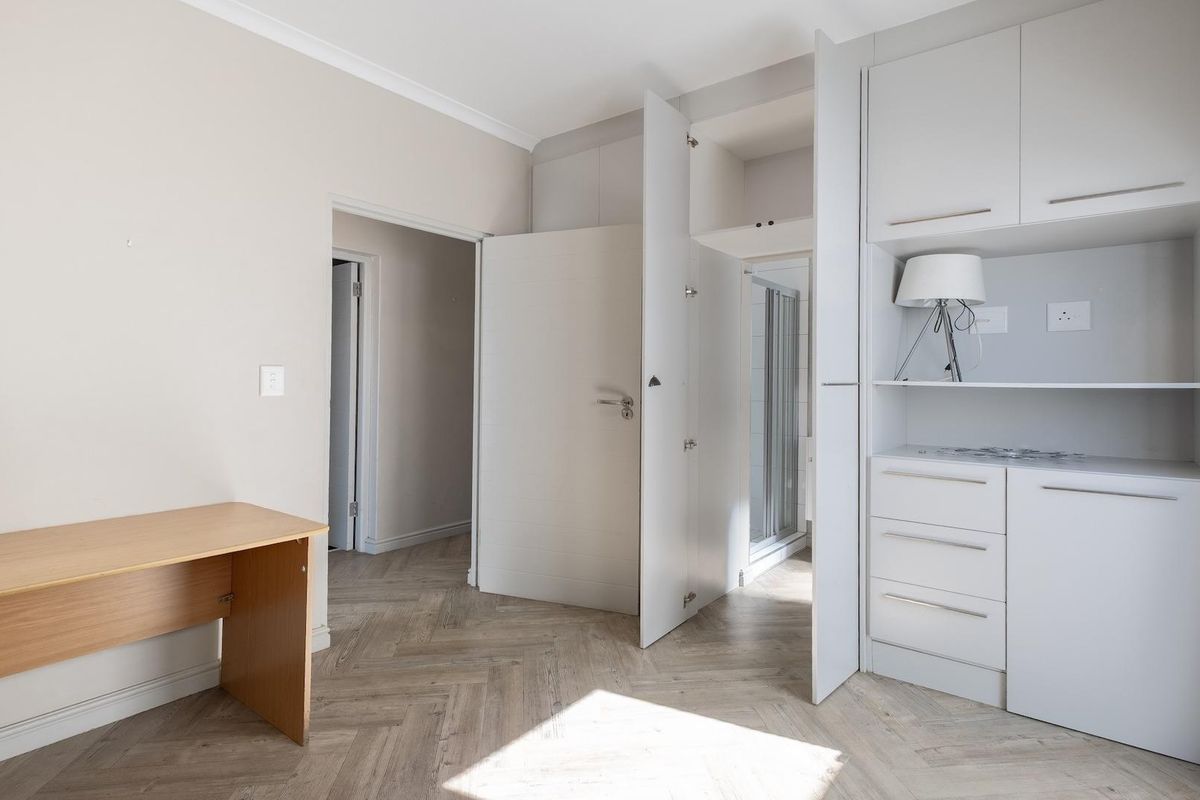 A bright bedroom featuring light wood-look herringbone flooring, built-in cabinetry with integrated shelving, and direct access to an en-suite bathroom.