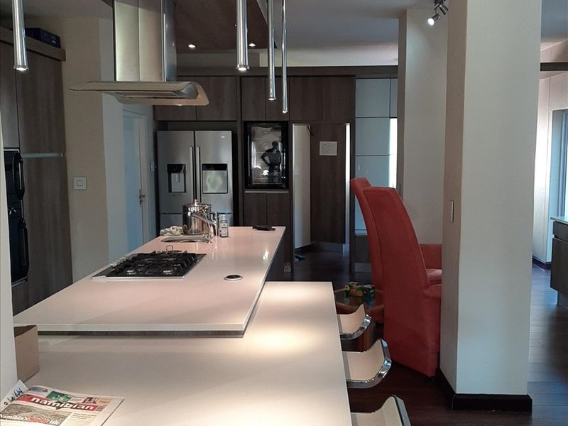 Modern kitchen featuring a large island with a gas hob, integrated cabinetry, stone countertops, and stylish pendant lighting in an open-plan layout.