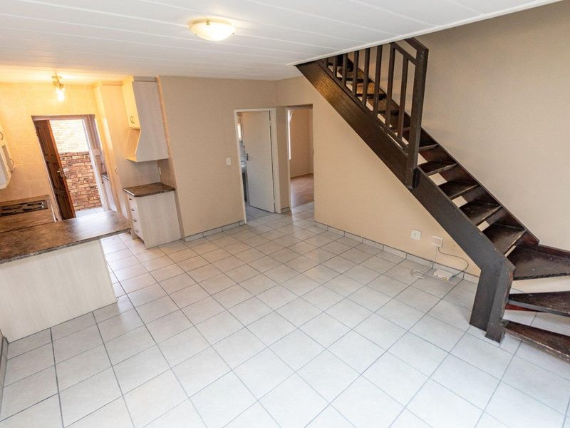 Open plan living area featuring tiled floors, a functional kitchen with built-in cabinetry, and a staircase leading to the upper level.