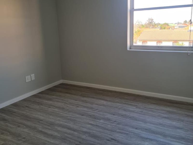 A clean, empty office space featuring modern grey laminate flooring, a suspended ceiling, and a window providing natural light and neighborhood views.
