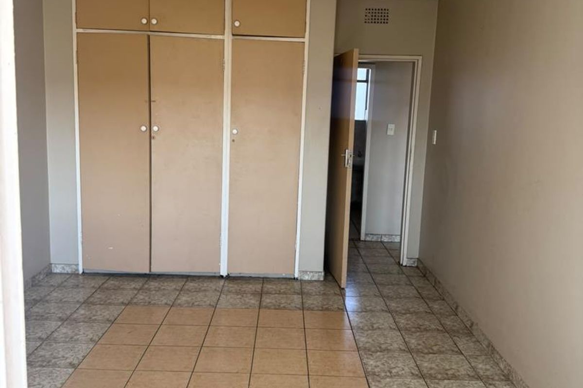 An empty bedroom featuring built-in cupboards and tiled flooring, offering a blank canvas for potential renovation or interior design updates.