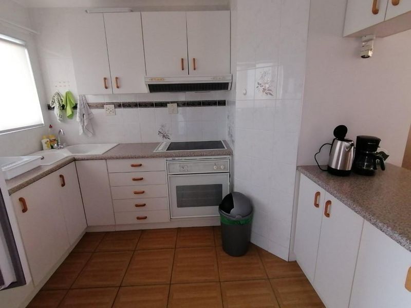 A functional kitchen featuring white built-in cabinetry, laminate countertops, tiled backsplash, and integrated cooking appliances with ceramic floor tiles.