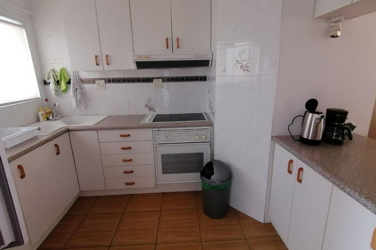 A functional kitchen featuring white built-in cabinetry, laminate countertops, tiled backsplash, and integrated cooking appliances with ceramic floor tiles.
