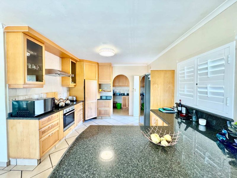Spacious kitchen featuring wooden cabinetry, granite countertops, built-in oven, extractor fan, and tiled flooring, with an adjacent scullery area visible through the archway.