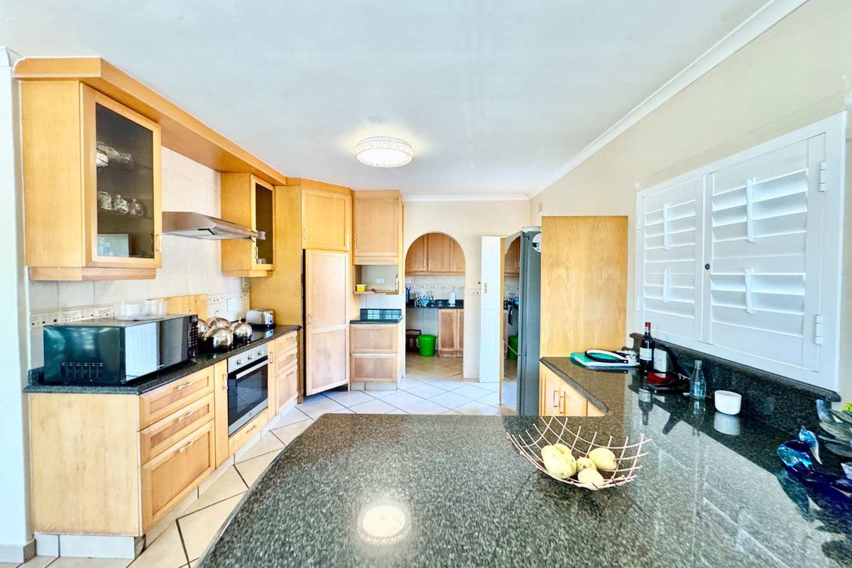 Spacious kitchen featuring wooden cabinetry, granite countertops, built-in oven, extractor fan, and tiled flooring, with an adjacent scullery area visible through the archway.