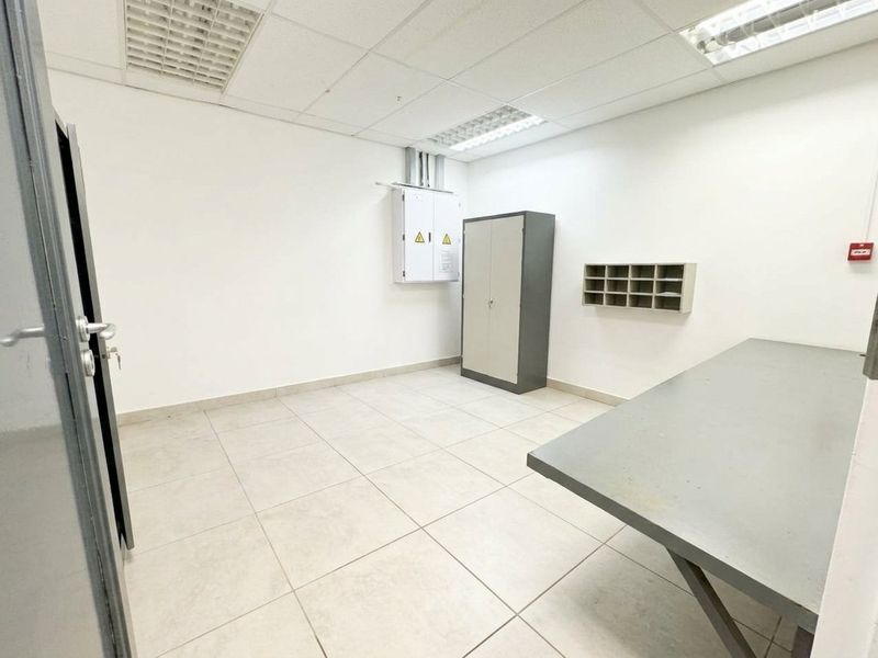 A functional utility or storage room featuring tiled flooring, suspended ceiling with recessed lighting, and wall-mounted electrical infrastructure.