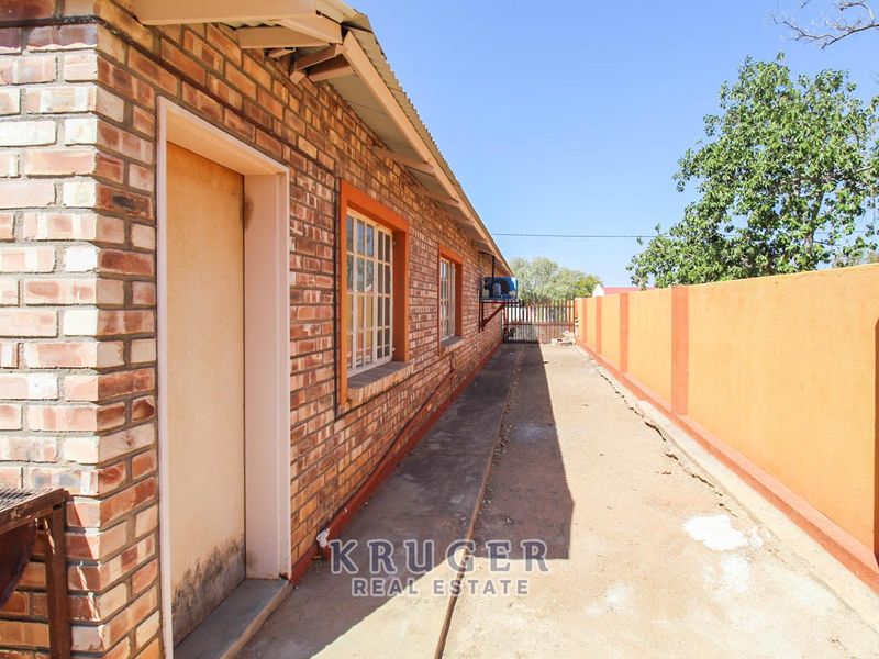 A side exterior view of the property featuring face brick walls, a concrete pathway, and a perimeter boundary wall.