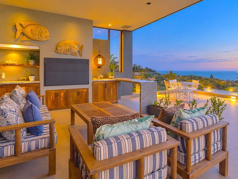 Spacious covered patio featuring built-in cabinetry, stone bar counter, and glass balustrades, offering expansive ocean views and seamless indoor-outdoor flow.