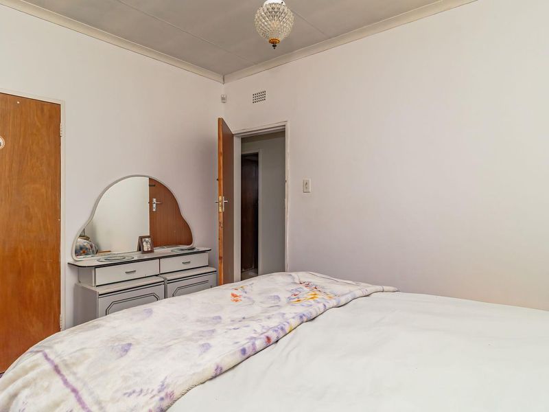 A functional bedroom featuring a built-in wooden cupboard, neutral wall finishes, and a central ceiling light fixture.