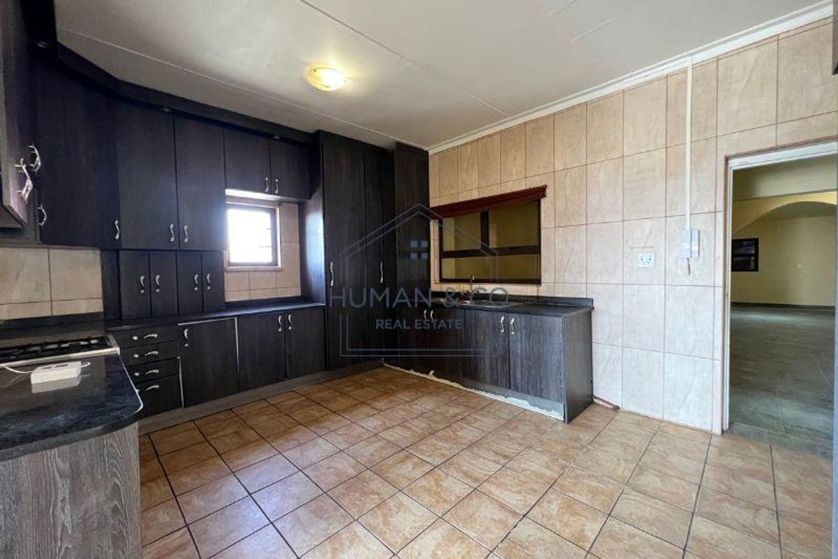 A functional kitchen featuring dark wood cabinetry, granite-look countertops, and tiled flooring, offering ample storage and workspace for daily meal preparation.