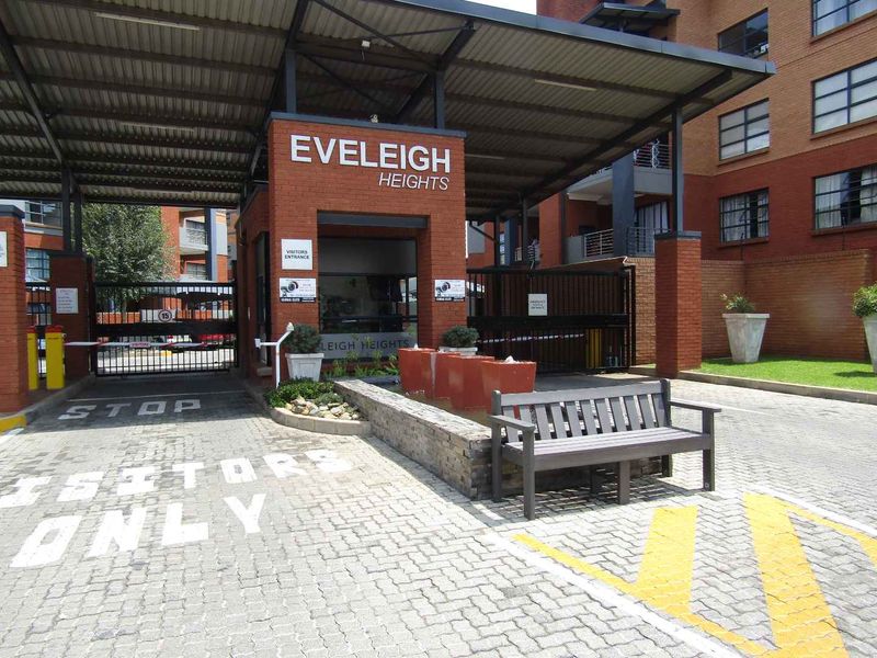 The main entrance to Eveleigh Heights apartment complex, featuring a secure gated access point, brick facade, and paved visitor parking area.