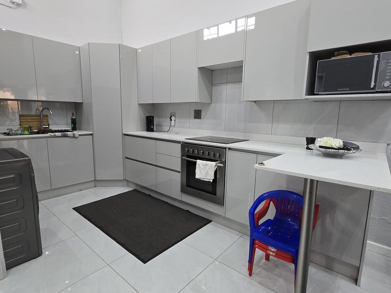 Modern kitchen featuring high-gloss cabinetry, stone countertops, integrated oven and hob, and a convenient breakfast bar area with tiled flooring.