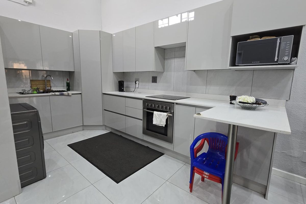 Modern kitchen featuring high-gloss cabinetry, stone countertops, integrated oven and hob, and a convenient breakfast bar area with tiled flooring.