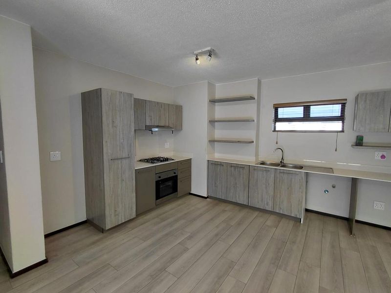 A modern, clean kitchen featuring light wood-grain cabinetry, stone countertops, a gas hob, and integrated oven, offering a functional and bright workspace.