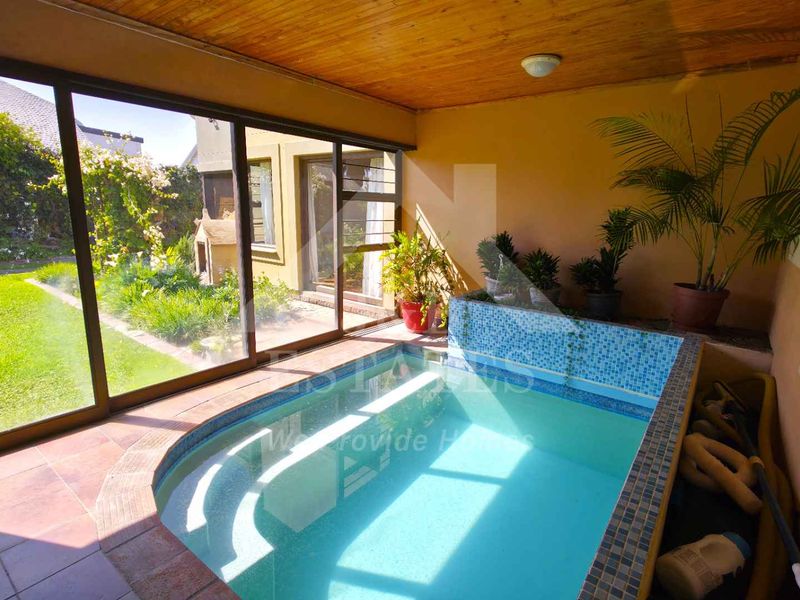 An indoor swimming pool area featuring mosaic tiling, tiled floors, and large sliding glass doors opening to the garden.