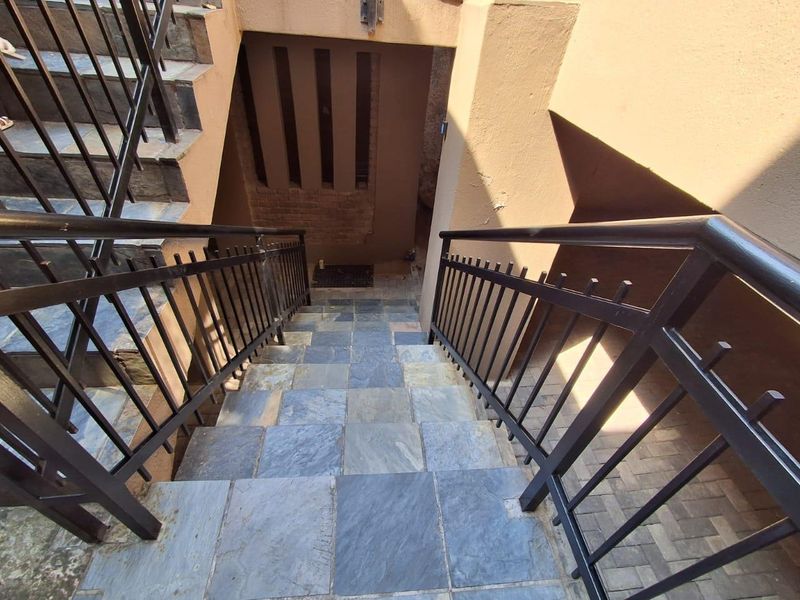 An outdoor stone-tiled staircase featuring metal balustrades leading down to a lower level with a brick feature wall.