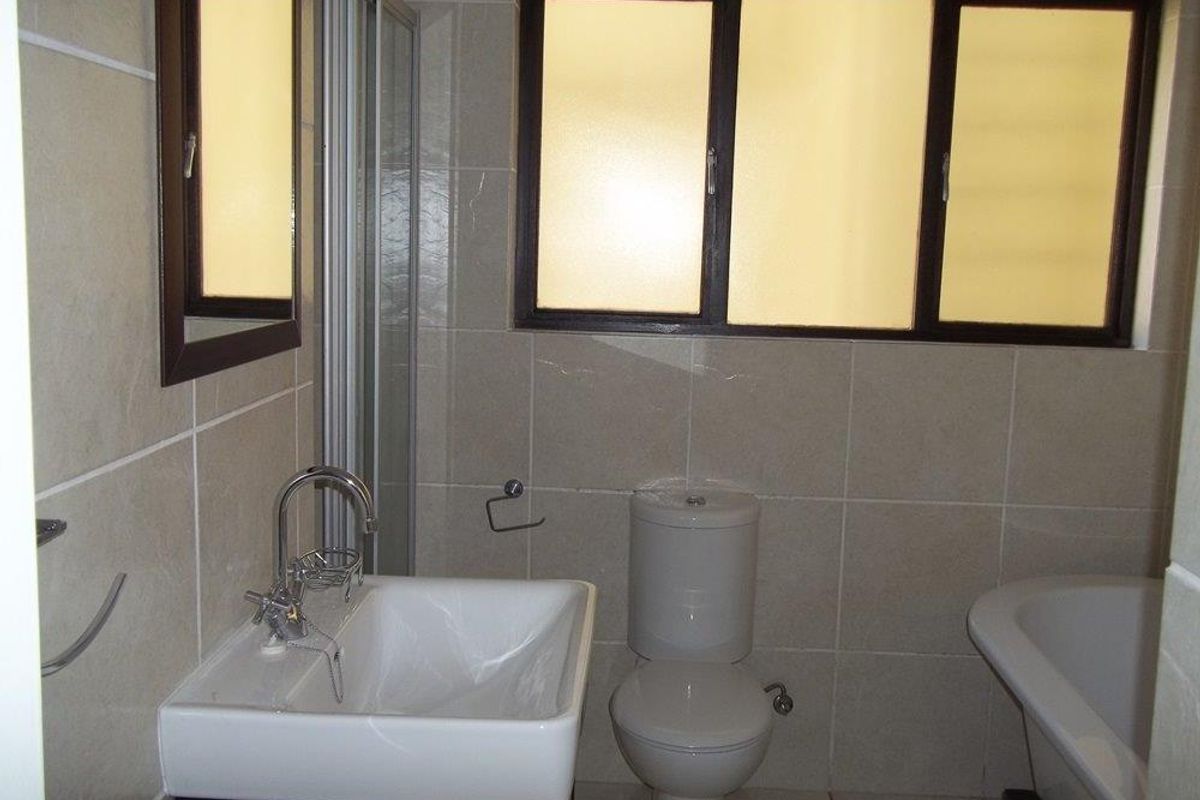 A functional bathroom featuring neutral wall tiles, a modern vanity basin, a toilet, and a bathtub with a shower screen.
