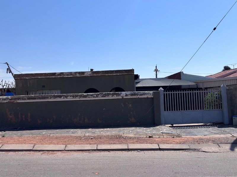 Front view of the property featuring a boundary wall, metal driveway gate, and paved entrance area.