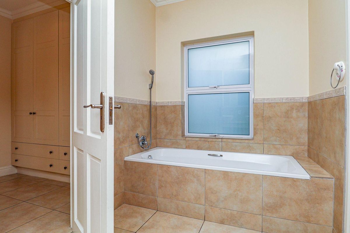 A functional bathroom featuring a built-in bathtub with tiled surround, frosted window, and adjacent built-in cabinetry in the dressing area.