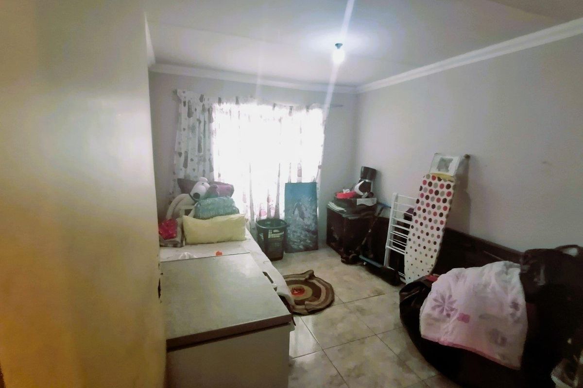 A small bedroom or utility space featuring tiled flooring and a window with curtains, currently used for storage.