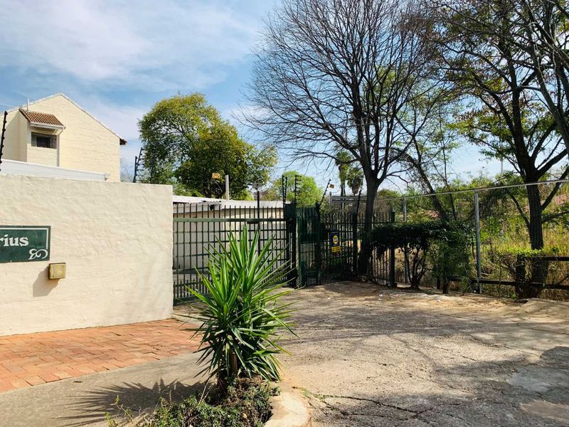 Front entrance view of the property featuring a paved driveway, secure metal gate, and perimeter wall with electric fencing.