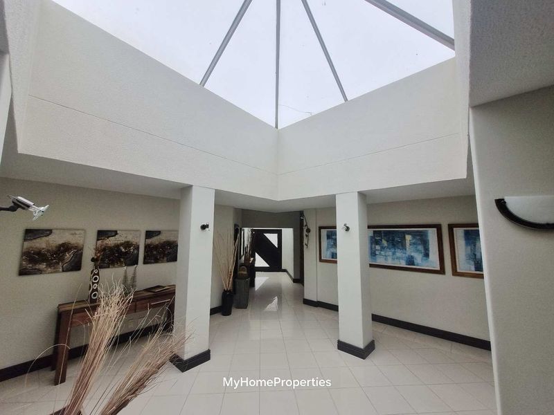 Spacious entrance hall featuring a large pyramid skylight, tiled flooring, and structural columns, creating a bright and welcoming foyer area.