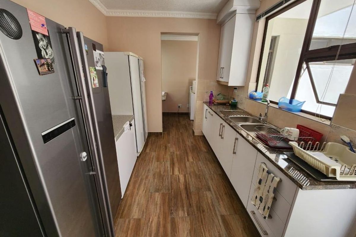 A functional kitchen featuring white cabinetry, granite-look countertops, a double stainless steel sink, and wood-look floor tiles.