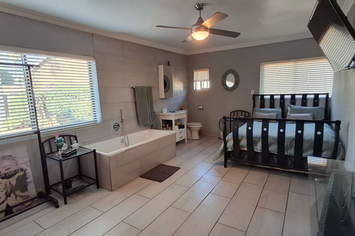 Spacious bedroom featuring an integrated bathtub, tiled flooring, ceiling fan, and a private toilet area, offering a unique open-plan layout.