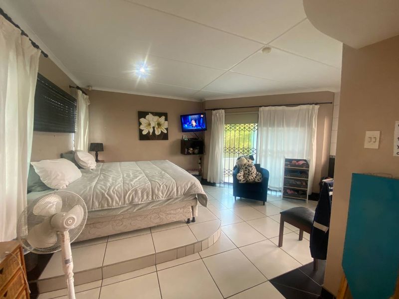 Spacious bedroom featuring a raised platform area, tiled flooring, and a sliding door leading to an outdoor space with a security gate.