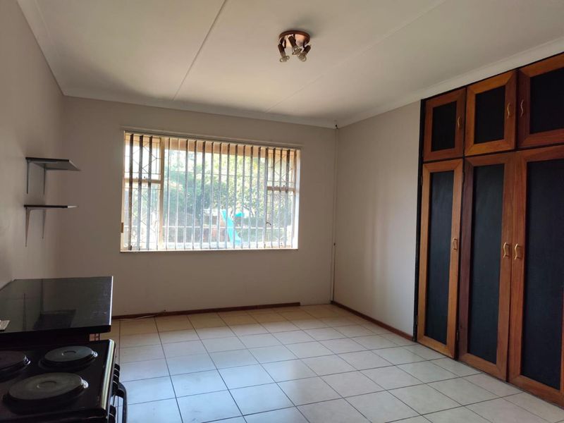 A functional kitchen featuring tiled flooring, built-in wooden cabinetry, and a window with security bars, offering a blank canvas for potential updates.