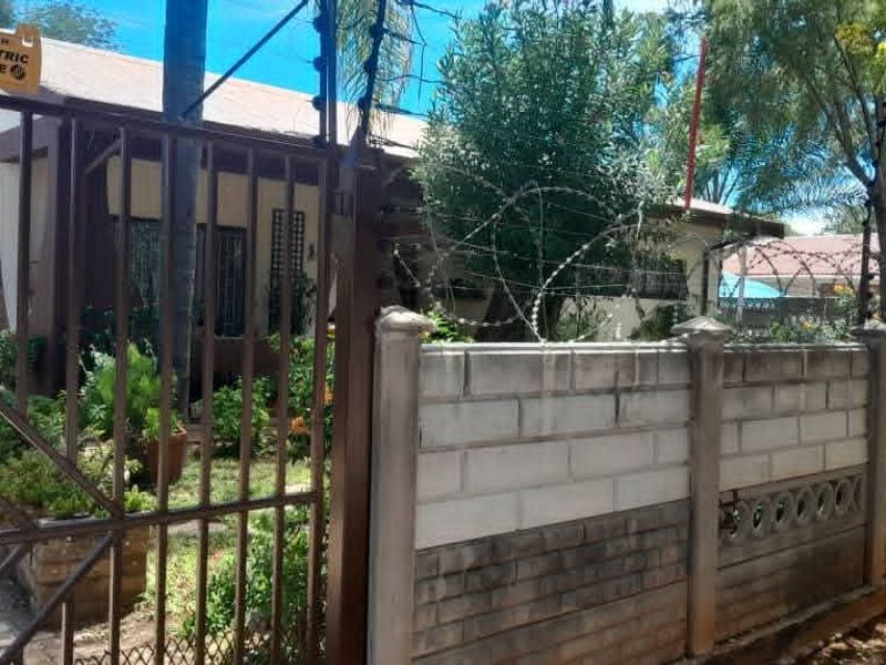 Front view of the property featuring a secure perimeter wall with electric fencing, razor wire, and a metal entrance gate.