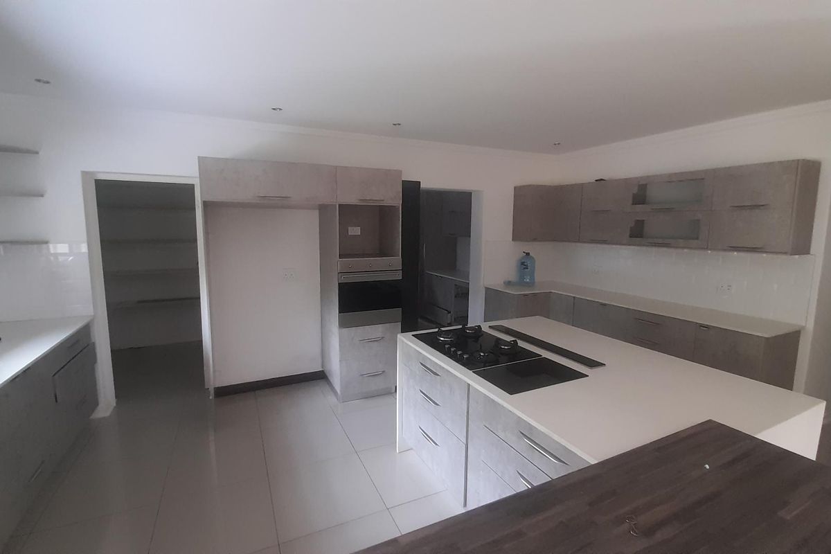 Modern kitchen featuring a central island with a built-in gas hob, stone countertops, ample cabinetry, and an adjacent walk-in pantry.