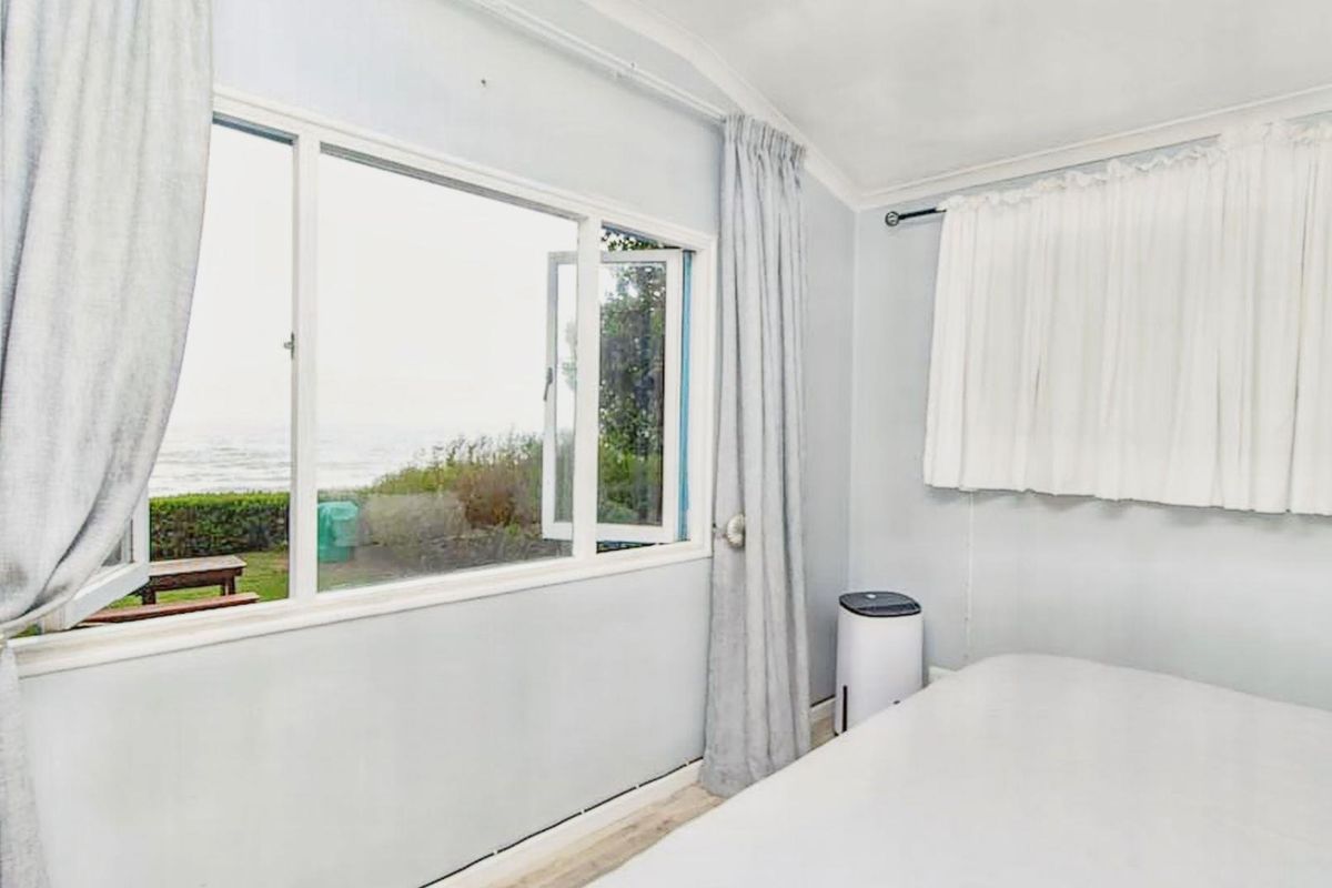 A bright bedroom featuring large windows with ocean views, neutral wall finishes, and simple window treatments.