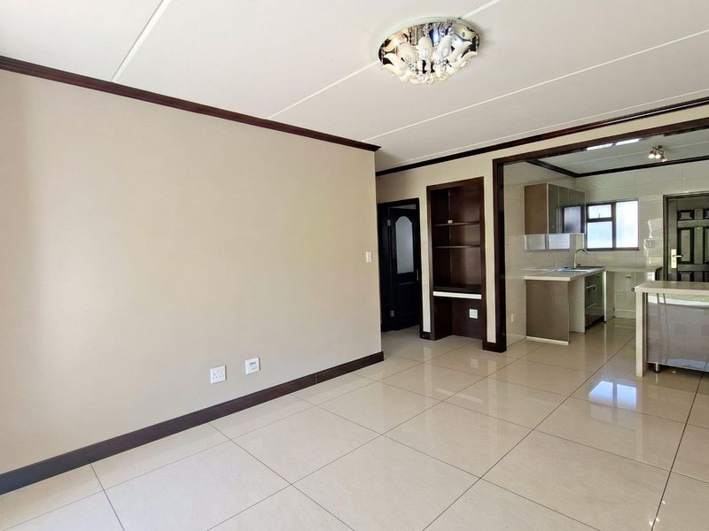 An open-plan living and kitchen area featuring neutral tiled flooring, built-in cabinetry, and a functional layout suitable for modern living.