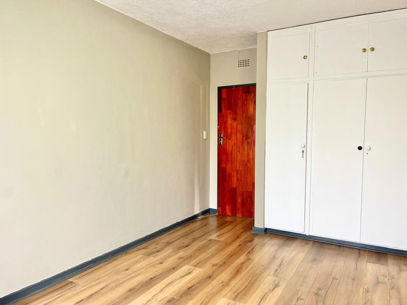 An empty bedroom featuring laminate flooring, built-in white cupboards, and a wooden internal door, offering a blank canvas for personalization.